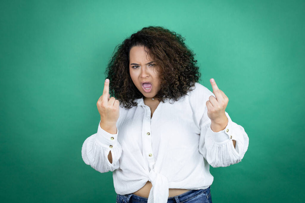 Молодая африканская американка в белой рубашке на зеленом фоне показывает средний палец делает трахнуть вас плохое выражение лица, провокация и грубое отношение. Крики возбужденных - Фото, изображение