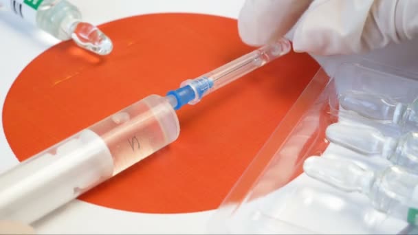 Шприц с ковидом-19 вакцина удерживается вручную в перчатке на фоне японского флага, вакцина против коронавируса, вакцинация в Японии начать концепцию - Кадры, видео