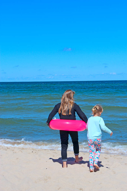 Dzieci pływają w morzu. Siostry cieszące się wakacjami. Szczególne momenty w 2021 roku. Odpocznij na morzu. Szczęśliwego dzieciństwa w kurorcie. Dzieci relaksujące się gumowym kółkiem na morzu podczas wakacji - Zdjęcie, obraz
