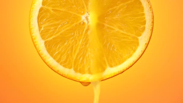 suco de laranja espremido na hora flui a partir da fatia de fruta madura fechar-se em um fundo laranja - Filmagem, Vídeo