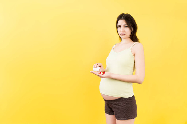 Elinde şişesi olan hamile bir kadın ve ellerinde renkli arkaplanda fotokopi alanı olan bir yığın hap var. Sağlık hizmetleri kavramı. - Fotoğraf, Görsel
