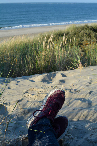 Відпочиваючи між дюнами, лежачи на пляжі з кросівками, з видом на море на узбережжі Північного моря в Нідерландах. - Фото, зображення