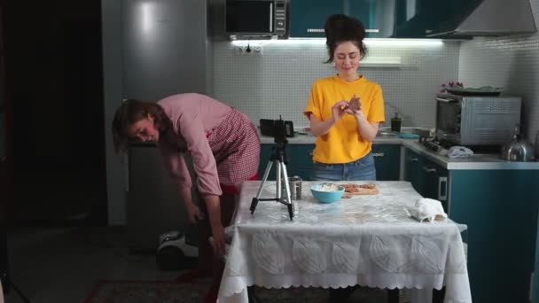 Дівчинка-підліток записує відео-блог для приготування їжі, пряникову трансляцію на смартфоні, показуючи пряники. Поруч мати в фартусі вакуумує. Концепція відеоблогів підлітків
 - Кадри, відео