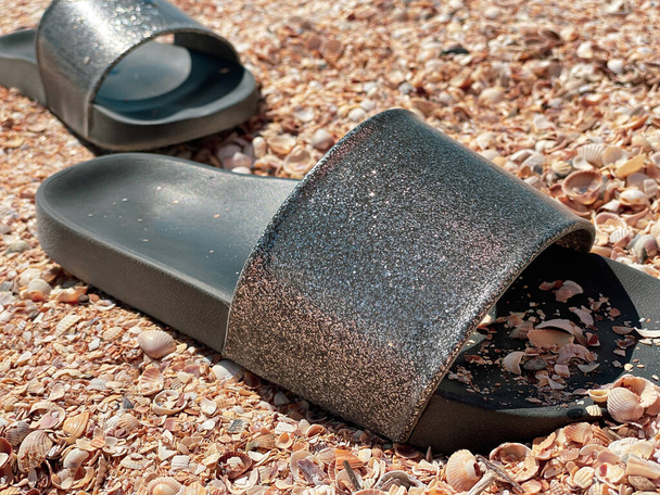 Zapatillas de playa con suelas negras y soporte superior plateado brillante de cerca en una playa de guijarros.  - Foto, imagen
