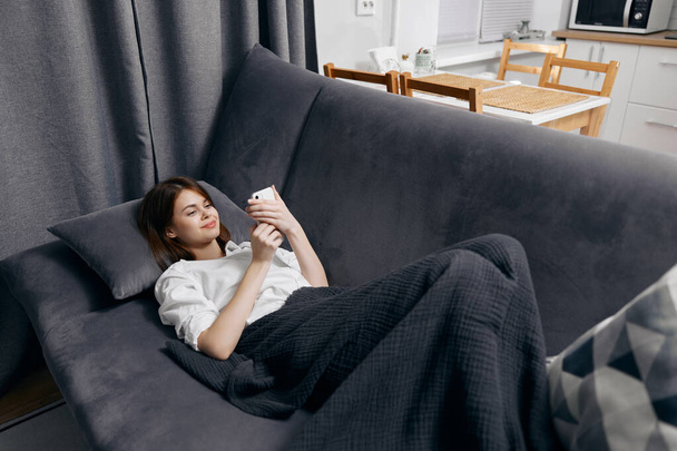 žena bílé tričko s telefonem v ruce leží na gauči - Fotografie, Obrázek