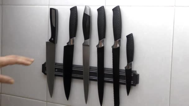 A mão do homem seleciona o item desejado de um conjunto de facas em uma faixa magnética. Um conjunto de facas na cozinha. - Filmagem, Vídeo
