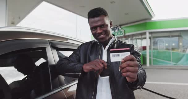 Портрет африканця на газовій станції з кавою в руках. Чоловік тримає пластикову картку на знижці в магазині і вказує на камеру. Заправлення автомобіля під час подорожі, зупинка GAS - Кадри, відео