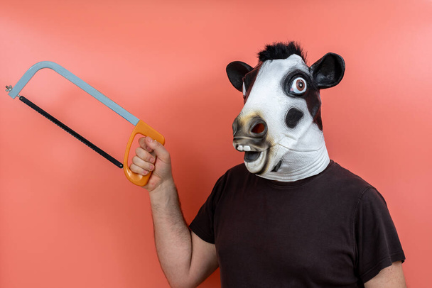 persona disfrazada con una máscara de cabeza de vaca sosteniendo una sierra con fondo rosa - Foto, imagen
