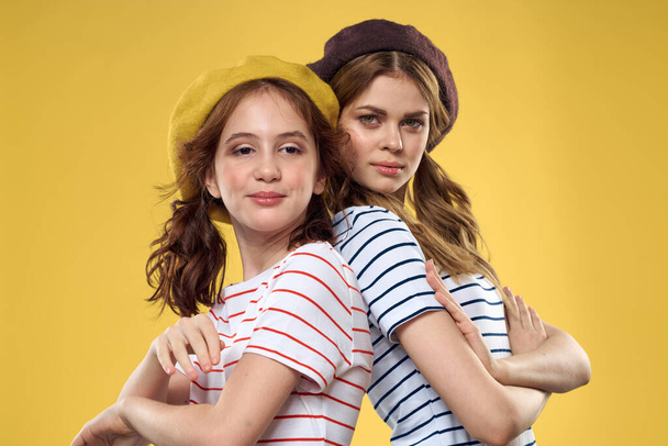Cheerful sisters in hats striped T-shirts joy lifestyle yellow background family - Fotoğraf, Görsel