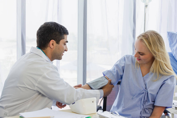 mannelijke arts zet een manchet van een bloeddrukmeter op vrouwelijke patiënt in de ziekenhuiskamer - Foto, afbeelding
