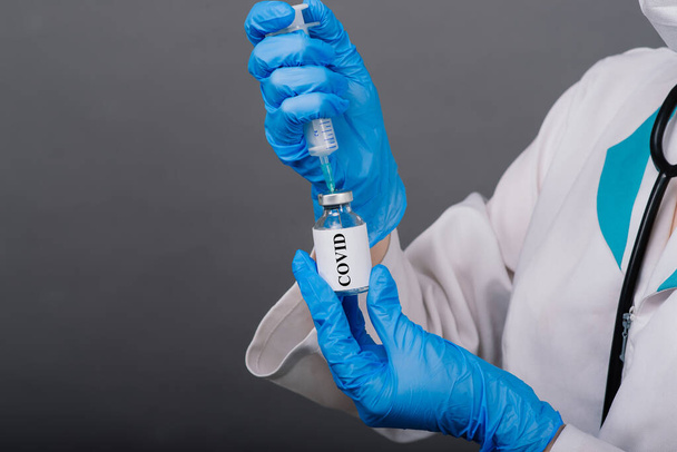 Elinde şırınga ve aşı tutan tıbbi maskeli ciddi bir kadın doktor gri renkte izole edilmiş. - Fotoğraf, Görsel