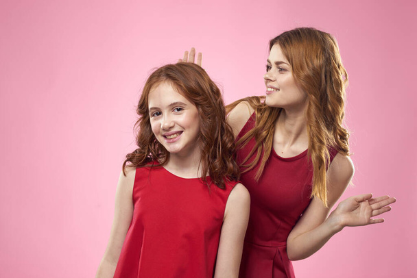 Fröhliche Mutter und Tochter in roten Kleidern stehen neben fröhlicher Familie auf rosa Hintergrund - Foto, Bild