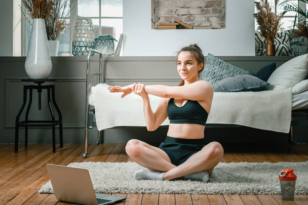 The young woman goes in for sports at home. Cheerful sportswoman with black hair resting on the floor at home,  watches a movie and studies from a laptop    in the bedroom - Photo, Image
