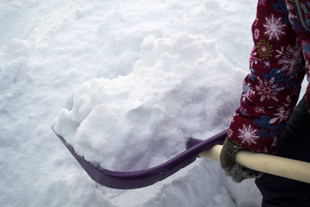 Ένα κορίτσι ρίχνει χιόνι με ένα μεγάλο πόδι. - Φωτογραφία, εικόνα