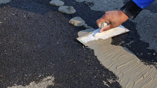 Sıvacı adamın elini kapat. İşçi çatlak yolu onarmak için bir çimento malası kullandı. Kopya alanı olan asfalt bir arka planda. Seçici odak - Fotoğraf, Görsel