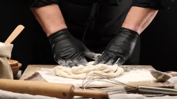 chef en guantes de látex negro amasando masa de harina de trigo blanco en una tabla de madera, preparando masa de pizza - Imágenes, Vídeo