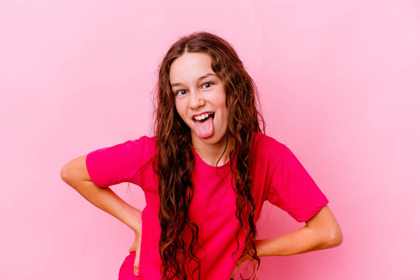 Pequeña chica caucásica aislada sobre fondo rosa divertida y amigable sobresaliendo lengua. - Foto, imagen