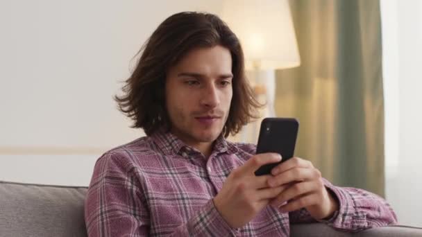 Közelkép portré fiatal férfi sms online okostelefon, ül otthon egyedül - Felvétel, videó