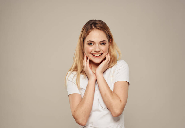 Mujer emocional en una camiseta blanca gestos con las manos y se ríe sobre un fondo beige. - Foto, imagen