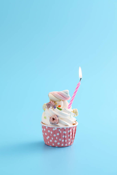 Kleurrijke cupcake met kaars geïsoleerd in blauwe achtergrond - Foto, afbeelding