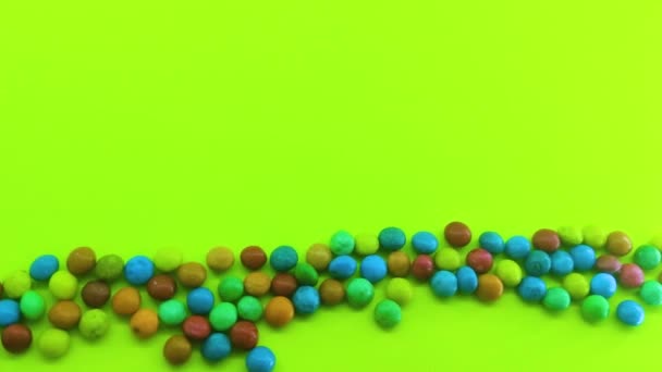 tło wielu kolorowych cukierków lub czekoladek w szkliwie na zielonym tle - Materiał filmowy, wideo