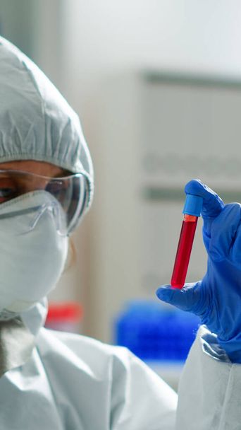Bioquímico em macacão segurando amostra de sangue analisando reação química - Foto, Imagem