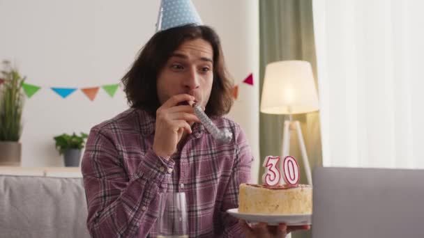 Boldog 30. születésnapot. Fiatal férfi ünnepli nyaralás online barátaival, fúj a laptop kamera és pezsgőt iszik - Felvétel, videó