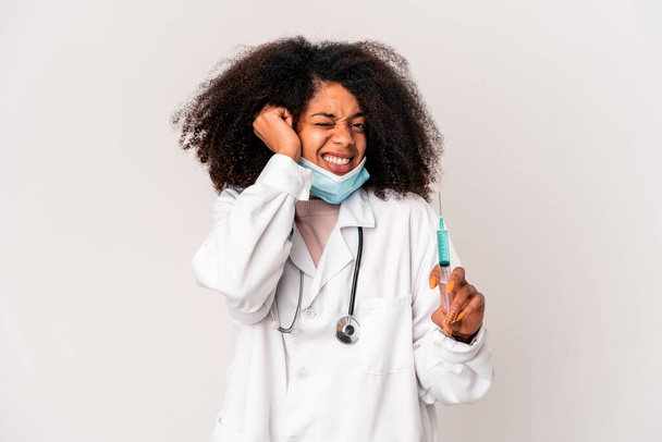 Jovem africana americana curly médico mulher segurando uma seringa cobrindo orelhas com as mãos. - Foto, Imagem