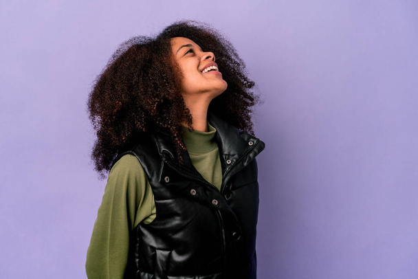Young african american curly woman isolated on purple background relaxed and happy laughing, neck stretched showing teeth. - Photo, Image