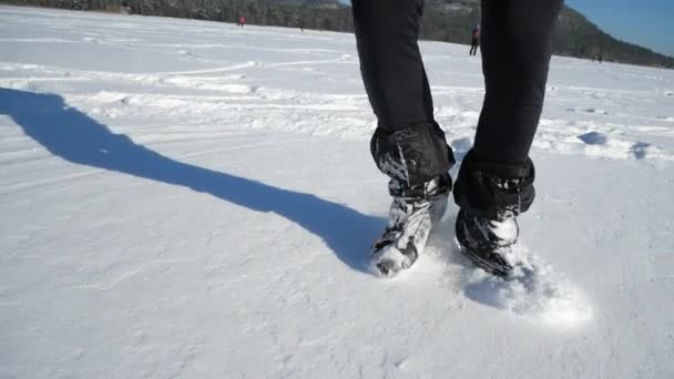 Nohy bruslař při bruslení na venkovním zasněženém ledu. Nízké zimní slunce ozařuje led. Temné stíny a dlouhé stíny na povrchu. Sportovní pohyby. Zpomalený pohyb 180fps - Záběry, video
