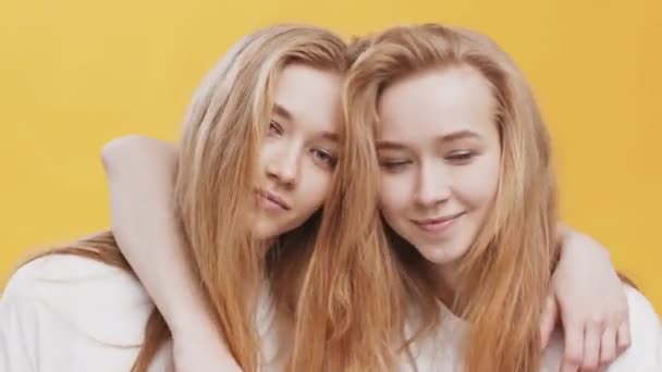 De cerca retrato de dos jóvenes pelirroja hermana gemela abrazando y mostrando el gesto de paz a la cámara, fondo de estudio naranja - Imágenes, Vídeo