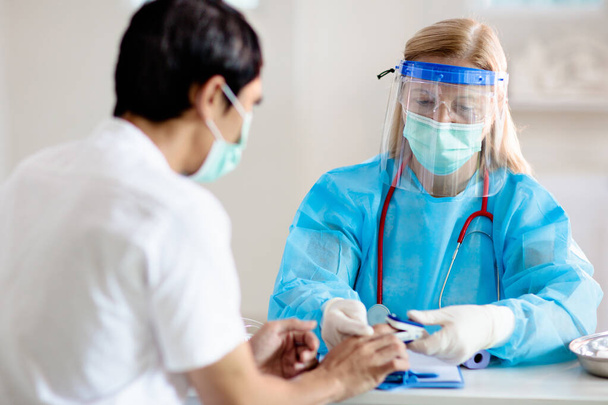 医師は、コロナウイルスの病気患者を調べる。健康診療所で顔マスクをしたアジア人の男が検査とスクリーニングを受ける。ウイルスの治療。コロナウイルスのパンデミック。COVID-19発生。咳、胸の痛み. - 写真・画像
