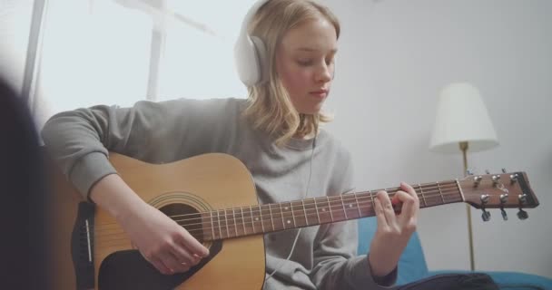 Το χαρούμενο κορίτσι πιάνει μια χορδή κιθάρας με τα δάχτυλά της με το αριστερό της χέρι. Μια γυναίκα με ακουστικά ακούει μουσική. - Πλάνα, βίντεο