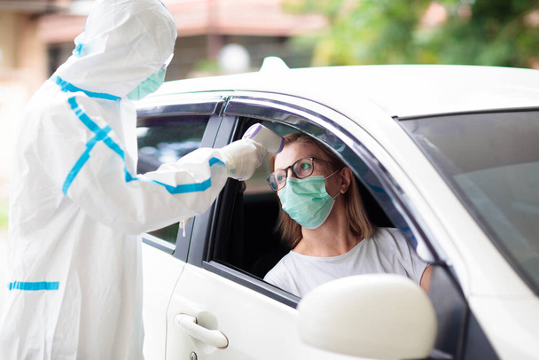 Coronavirus nasal drive-through swab test. Doctor in hazmat suit taking saliva sample for covid-19 diagnostics in a car. Woman driver patient at drive-thru testing station in hospital. Virus outbreak. - Photo, Image