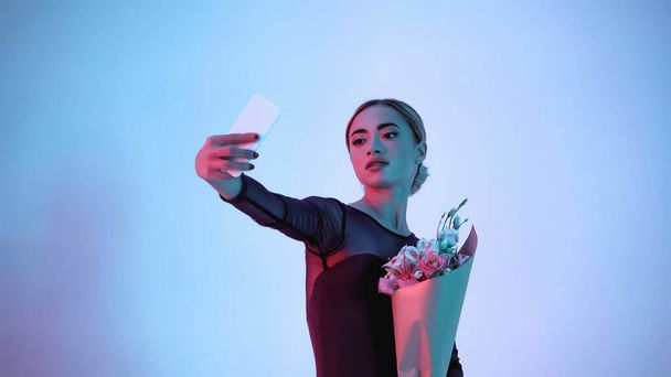 young ballerina holding flowers while taking selfie on blue - Foto, Imagem