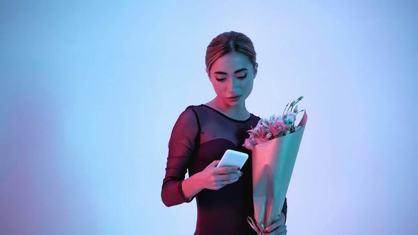 Ballerina hält Blumen während Smartphone auf blau  - Foto, Bild