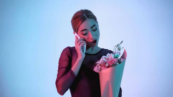 bailarina sosteniendo flores mientras habla en el teléfono inteligente en azul  - Foto, imagen
