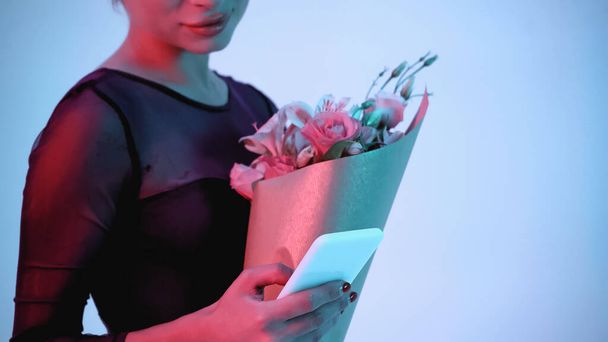 vista recortada de la bailarina sosteniendo teléfono inteligente y flores en azul  - Foto, imagen