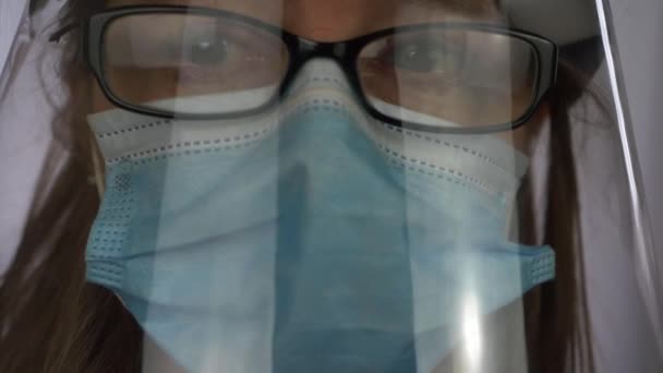 フェイスマスクとフェイスシールドを身に着けている女性医療スタッフは、カメラに見える - 映像、動画