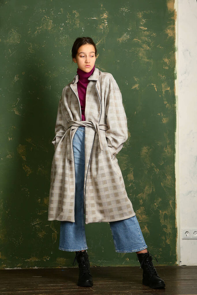 teen girl in checkered trench coat, jeans and bootswalking full body portrait on green wall background - Valokuva, kuva