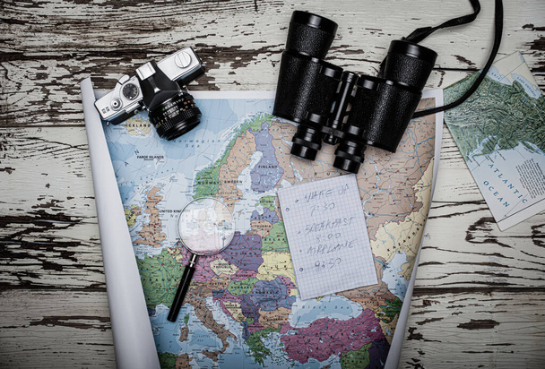 Επίπεδη απεικόνιση της έννοιας του ταξιδιωτικού σχεδιασμού. Κάτοψη σημειώματος από χαρτί, κιάλια και χάρτη της Ευρώπης σε ξύλινο τραπέζι - Φωτογραφία, εικόνα