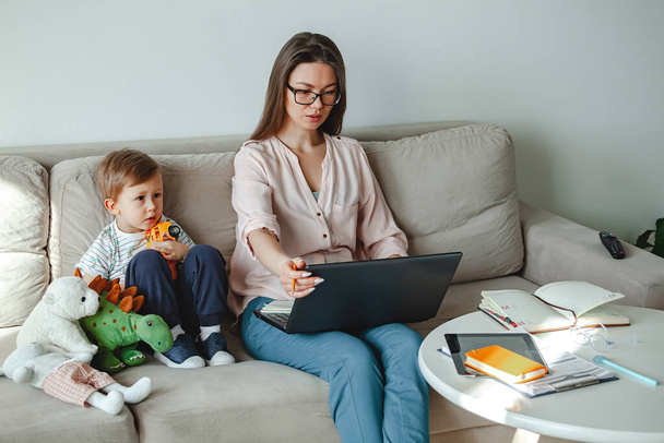 Έννοια της εργασίας στο σπίτι και κατ 'οίκον οικογενειακή εκπαίδευση, μητέρα που εργάζεται με φορητό υπολογιστή στο σπίτι, παιδί που παίζει κοντά - Φωτογραφία, εικόνα