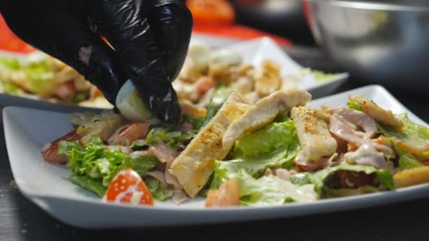 Männliche Hände legen die Hälfte der gekochten Wachteleier zum Kaisersalat in einen weißen Teller. Küchenchef in Handschuhen arrangiert köstliche Speisen für das Servieren. Konzept des Kochens von Lebensmitteln. Nahaufnahme Langsam mo - Filmmaterial, Video