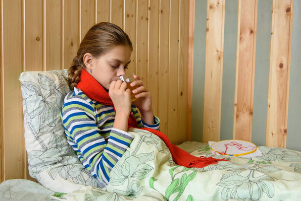 Chora dziewczyna pije herbatę siedząc w łóżku - Zdjęcie, obraz