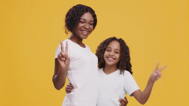 Fröhliche afrikanisch-amerikanische Mutter und Tochter zeigen Friedensgeste in die Kamera und umarmen sich auf orangefarbenem Hintergrund - Filmmaterial, Video