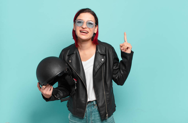 young attractive red hair woman feeling like a happy and excited genius after realizing an idea, cheerfully raising finger, eureka!. motorbike rider concept - Fotó, kép