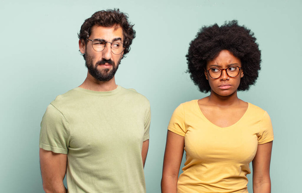 multiracial couple of friends feeling sad, upset or angry and looking to the side with a negative attitude, frowning in disagreement - Photo, image