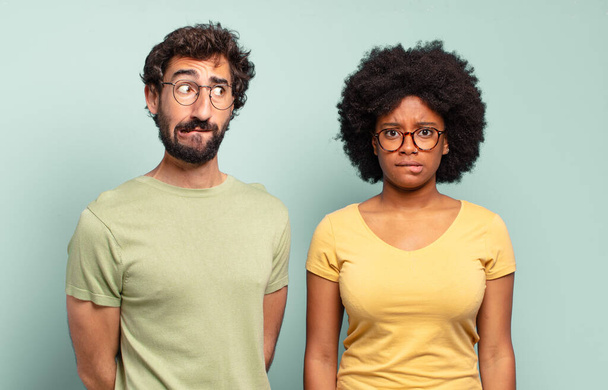 multiracial couple of friends looking puzzled and confused, biting lip with a nervous gesture, not knowing the answer to the problem - Photo, image