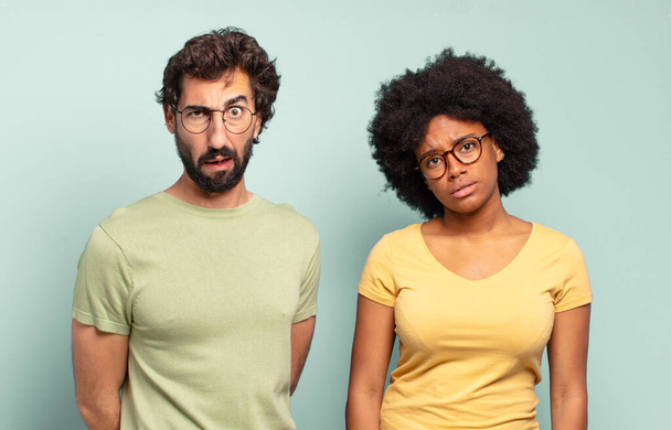 multiracial couple of friends feeling puzzled and confused, with a dumb, stunned expression looking at something unexpected - 写真・画像