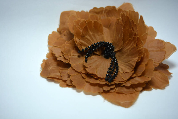 Il fiore marrone è realizzato in tessuto in modo caotico e decorato con piccole perline nere situate su uno sfondo bianco.  - Foto, immagini